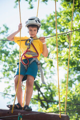 Boy in helmet doing rock climbing in rope park walking on ropeway overcoming obstacles