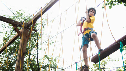 A child is engaged in rock climbing in a rope park in nature, walking along a cable car overcoming...