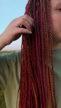 Beautiful young woman hairstyle with colorful hair extensions braid in thin braids and afro braids. Red dreadlocks close up