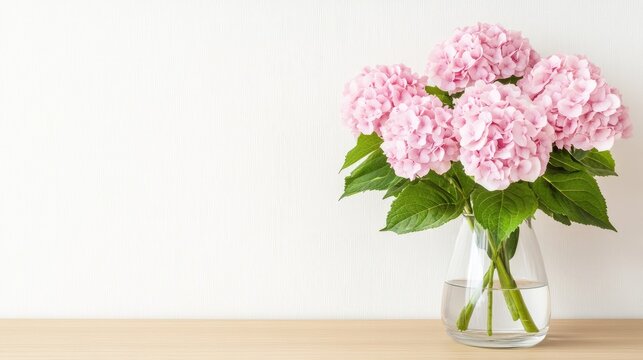 Delicate white hydrangea blooms create a fresh, elegant display in a clear vase on a wooden table against a soft gray backdrop