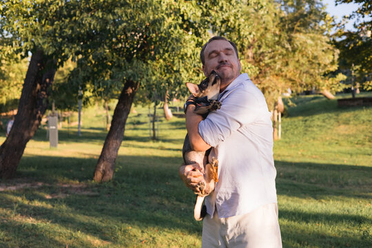 Smiling middle-aged man walks and plays with a small dog in public park