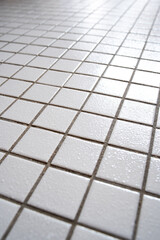 Small, white, ceramic tile flooring inside apartment bathroom, close up shot, no people