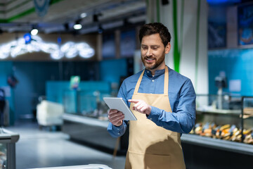 Supermarket employee in apron using digital tablet for inventory management. Image represents...