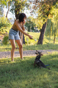 Smiling young woman walks and plays with a small dog in public park,