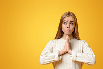 Cherished wish. Teen girl pleading for something, keeping hands together and biting lip over orange...
