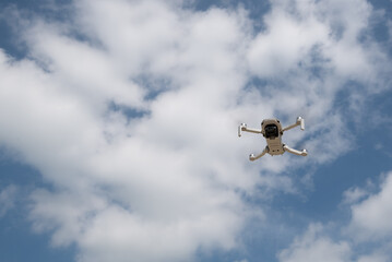 Low angle view of drone with camera flying over blue cloudy sky. Aerial photography and filming