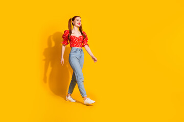 Full size photo of pretty young girl walking model wear trendy red outfit isolated on yellow color background