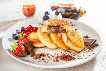 Cottage cheese pastries with strawberry, syrniki stuffed with chocolate on a white plate, selective focus