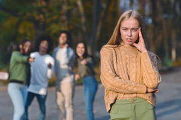 Upset blonde girl over laughing and pointing multiracial group of teenagers