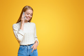 Modern communication. Coquette girl having pleasant phone conversation with somebody, orange studio background with free space