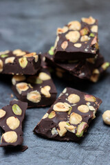 Pieces of dark chocolate with nuts on a gray background, top view, copy space. Homemade chocolate bar. Healthy eating concept. 
