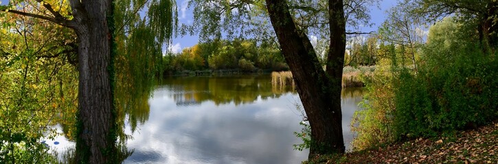 Panoramafoto von einem See mit grünen Ufern und Bäumen im Vordergrund