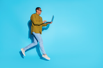 Full length photo of handsome young guy running hold netbook dressed stylish plaid garment isolated on blue color background