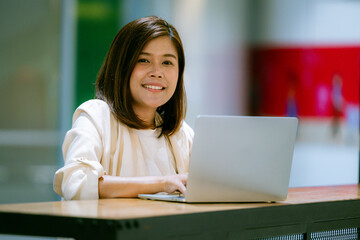 Smiling professional young Asian businesswoman talking in front of the camera having video conference with her business partners on laptop in a contemporary office space