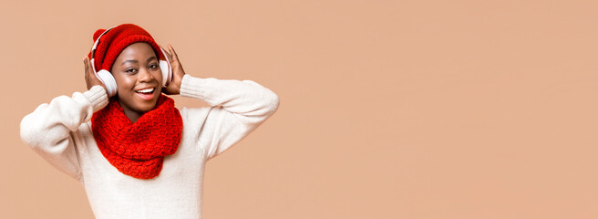 Emotional winter young african woman in wireless headphones listening to music and smiling at...