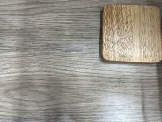 A light wooden square coaster placed on a matching wood grain surface, showcasing natural texture.