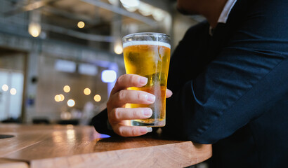 A close-up of a frothy, cold pint of golden beer in a transparent glass, set on a wooden table in a...
