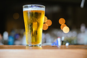 A close-up of a frothy, cold pint of golden beer in a transparent glass, set on a wooden table in a dimly lit pub, evoking a vintage, celebratory atmosphere.