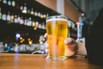 A close-up of a frothy, cold pint of golden beer in a transparent glass, set on a wooden table in a...