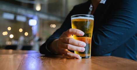 A close-up of a frothy, cold pint of golden beer in a transparent glass, set on a wooden table in a...