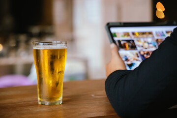 A close-up of a frothy, cold pint of golden beer in a transparent glass, set on a wooden table in a...