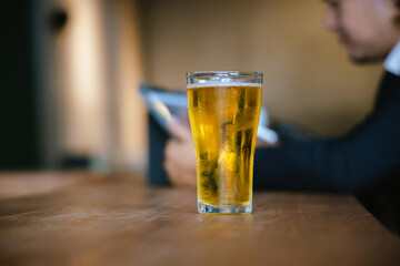 A man pours frothy beer into a glass at a lively pub. Friends gather around the bar, enjoying drinks and celebrating, with a warm, golden glow highlighting the joyful, friendly atmosphere.