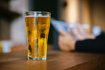A man pours frothy beer into a glass at a lively pub. Friends gather around the bar, enjoying drinks and celebrating, with a warm, golden glow highlighting the joyful, friendly atmosphere.