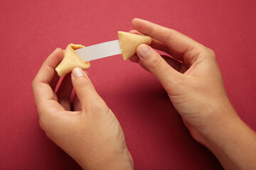 Woman holding tasty fortune cookie and paper with prediction on red background. Space for text