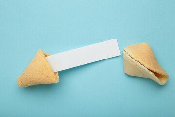 Cracked traditional fortune cookie with prediction on blue background. Top view