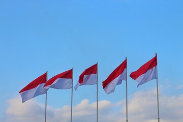 The Indonesian flag waving in the sky with a beautiful background of white fluffy clouds and blue sky.