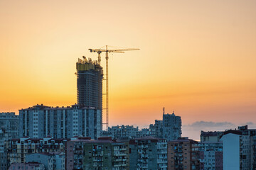 Skyscraper under construction with cranes at sunset. Construction site of new high-rise building. Urban development and growth of a city
