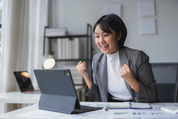 Young businesswoman is raising her fists in the air, feeling happy and excited about her success while working on a project in the office