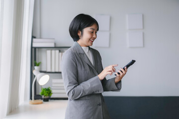 Young asian businesswoman smiles while using her smartphone in a modern office, showcasing confidence and success