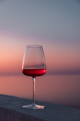 Close up shot of an elegant glass or chalice of rose wine with a beautiful sunset background. Pink sky, island life summer mood, elegance and wine tour or tasting.