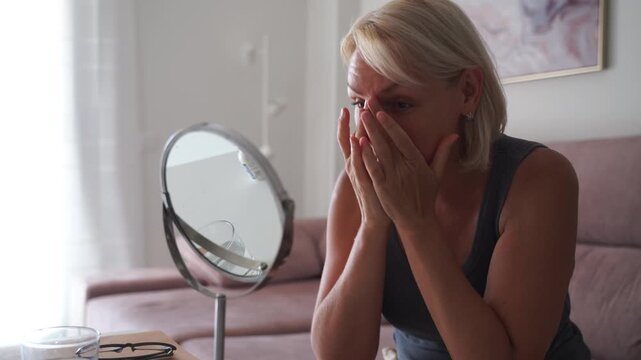  A senior woman carefully looking at her hair in a mirror while sitting in her living room, reflecting on self-care and aging