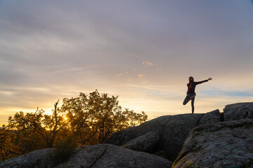 Silhouette of woman doing yoga and meditation at sunrise on top of a mountain in nature