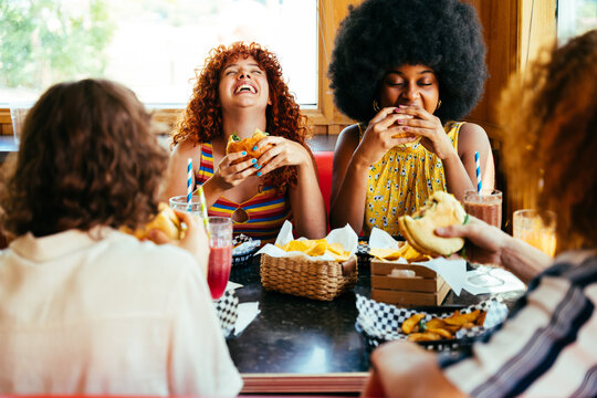 Multiethnic group of friends having meal at 80s vintage diner restaurant - Multiracial young people bonding and having fun, eating in an american fast food burger house