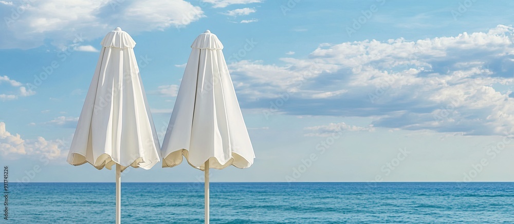 Poster Close up of two closed white canvas beach umbrellas set against a backdrop of the sea and a blue sky with clouds. with copy space image. Place for adding text or design
