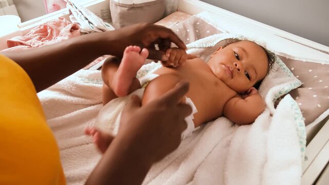 Mother doing baby legs and arms exercises to her baby girl changing table