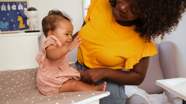 Mother changes her baby girl on a changing table in a nursery