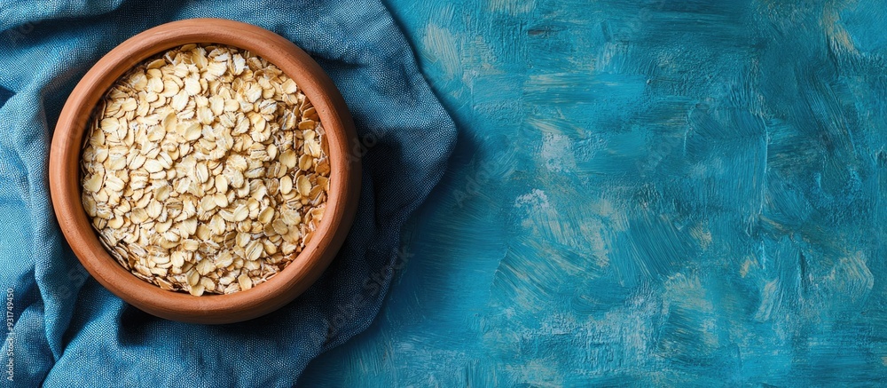 Poster oat flakes in a clay bowl on a blue linen napkin dry rolled oats on wooden boards healthy eating ide