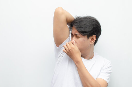 young asian man in white tshirt feeling embarrased because of his body odor. man smelling bad odor on his armpit.
