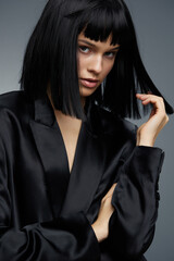 Woman with black hair in a black suit poses for the camera, hand on her head, eyes looking to the side, capturing a contemplative and stylish moment