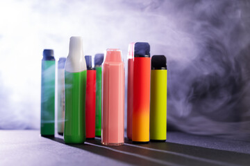 A set of colorful disposable electronic cigarettes of different shapes on a black background with...
