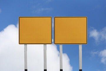 Empty yellow road sign with a background of blue sky and white clouds.