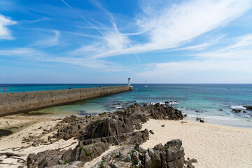 Vue sur le môle et le phare du Raoulic, avec en premier plan une plage de sable, des rochers et...