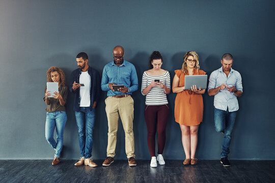 Technology, connectivity and group of business people at wall together with phone, tablet and laptop. Internet, communication and creative team with contact on website, digital network or mobile app