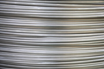 Close-up of coiled aluminum wires, highlighting their smooth surface and layered overlapping pattern, captured in soft lighting..