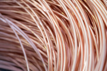 Close-up of coiled copper wires, showcasing their shiny surface and intricate overlapping pattern, captured in warm lighting..