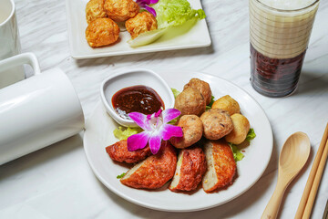 Assorted Fried Snacks with fish cake, Fried squid balls, Dipping Sauce, Taiwanese red bean ice tea served in dish isolated on marble background side view of taiwan food
